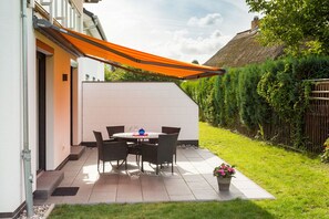 Eine Terrasse mit Tisch und Stühlen, einem Blumentopf und einer Struktur mit Strohdach.