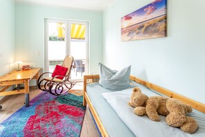 Ein Zimmer mit einem Bett, einem Schaukelstuhl, einem Tisch und einem Fenster mit Vorhängen.