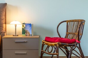 A wicker chair with a red cushion, a bedside table with a lamp, and a book titled 'Auszeit Unter Segeln' on the table. - 1,800 m to the beach, 2 bedrooms, sleeps up to 4, Wi-Fi, clothes drying rack (Breege)