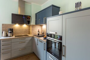 Een moderne keuken met een inbouwoven, een koffiezetapparaat en een fles wijn op het aanrecht.
