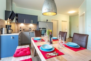 A modern kitchen with a dining area set for four, featuring a wooden table, blue plates, and a hanging light fixture. - 1,800 m to the beach, 2 bedrooms, sleeps up to 4, Wi-Fi, clothes drying rack (Breege)