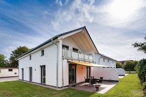 Ein modernes, zweistöckiges Haus mit Balkon, überdachter Terrasse und gepflegtem Rasen.