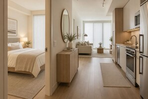 Ein modernes Hotelzimmer mit Bett, Nachttisch, Lampe und Blick auf den angrenzenden Wohnbereich.