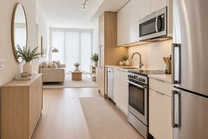 Eine moderne Küche mit Edelstahlgeräten, ein Essbereich mit einer Couch und ein großes Fenster mit Jalousien.