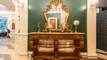 A grand hallway with a large ornate mirror, a wooden console table with drawers, and a chandelier.