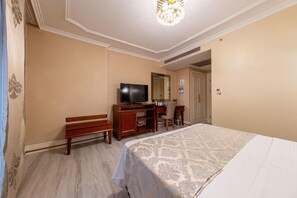 A hotel room with a bed, a desk, a television, and a bench.