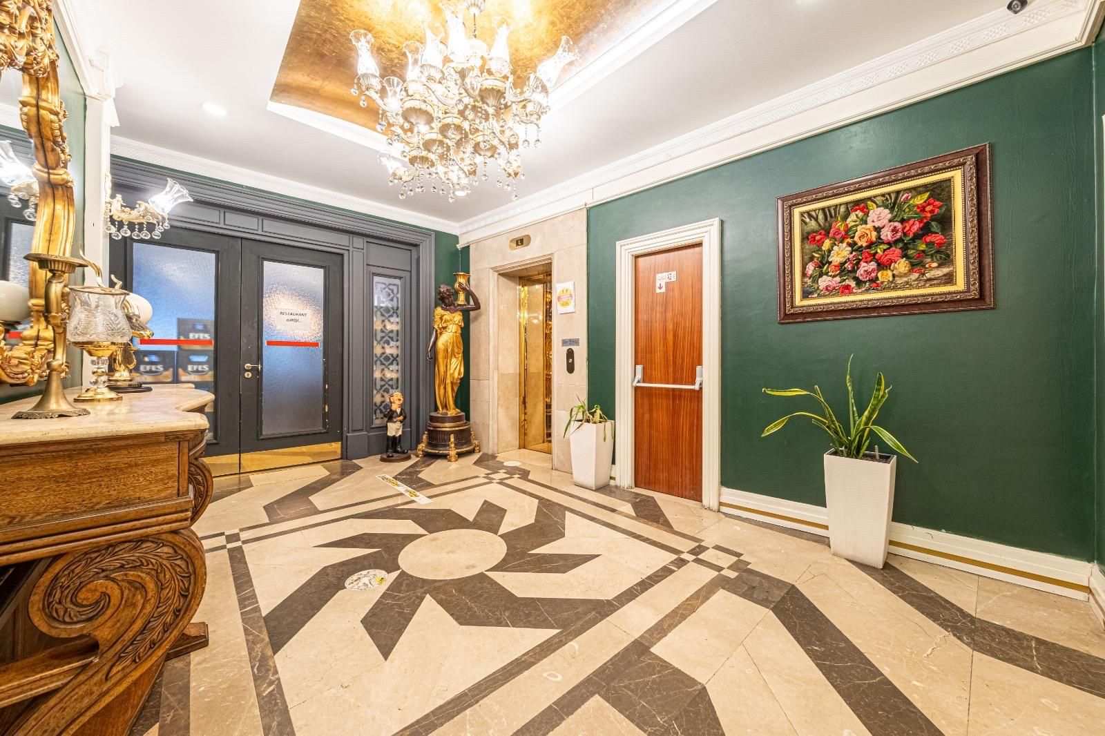 Um hall de entrada com piso de mármore, lustre, estátua, pintura e uma porta.