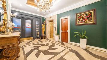 Um hall de entrada com piso de mármore, lustre, estátua, pintura e uma porta.
