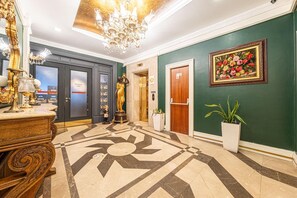 A lobby with a marble floor, a chandelier, a statue, a painting, and a door. - VELORA GRAND (Istanbul)