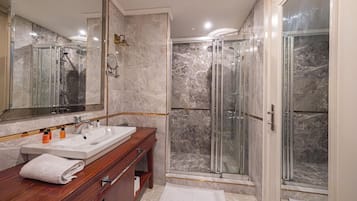 A modern bathroom with a marble shower enclosure, a double sink vanity, and a large mirror.