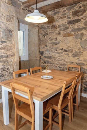 A rustic dining area with a wooden table and chairs, a pendant light, and a stone wall. - La Casita Azul | Seaside House in Malpica, Costa da Morte (Malpica)