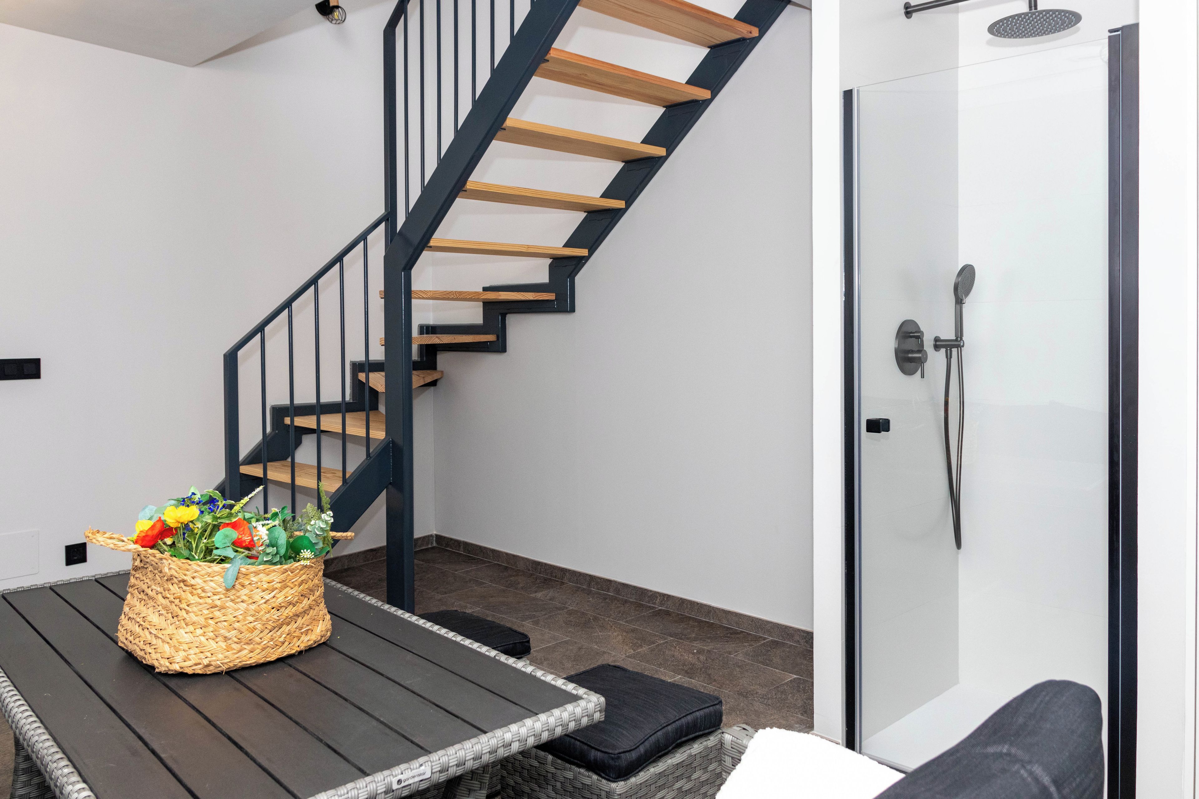 A modern interior with a wooden staircase, a wicker basket with flowers, and a glass shower enclosure.