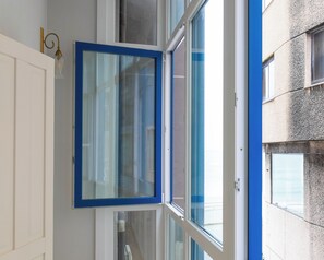 A room with a window, a white door, and a view of a building outside. - La Casita Azul | Seaside House in Malpica, Costa da Morte (Malpica)