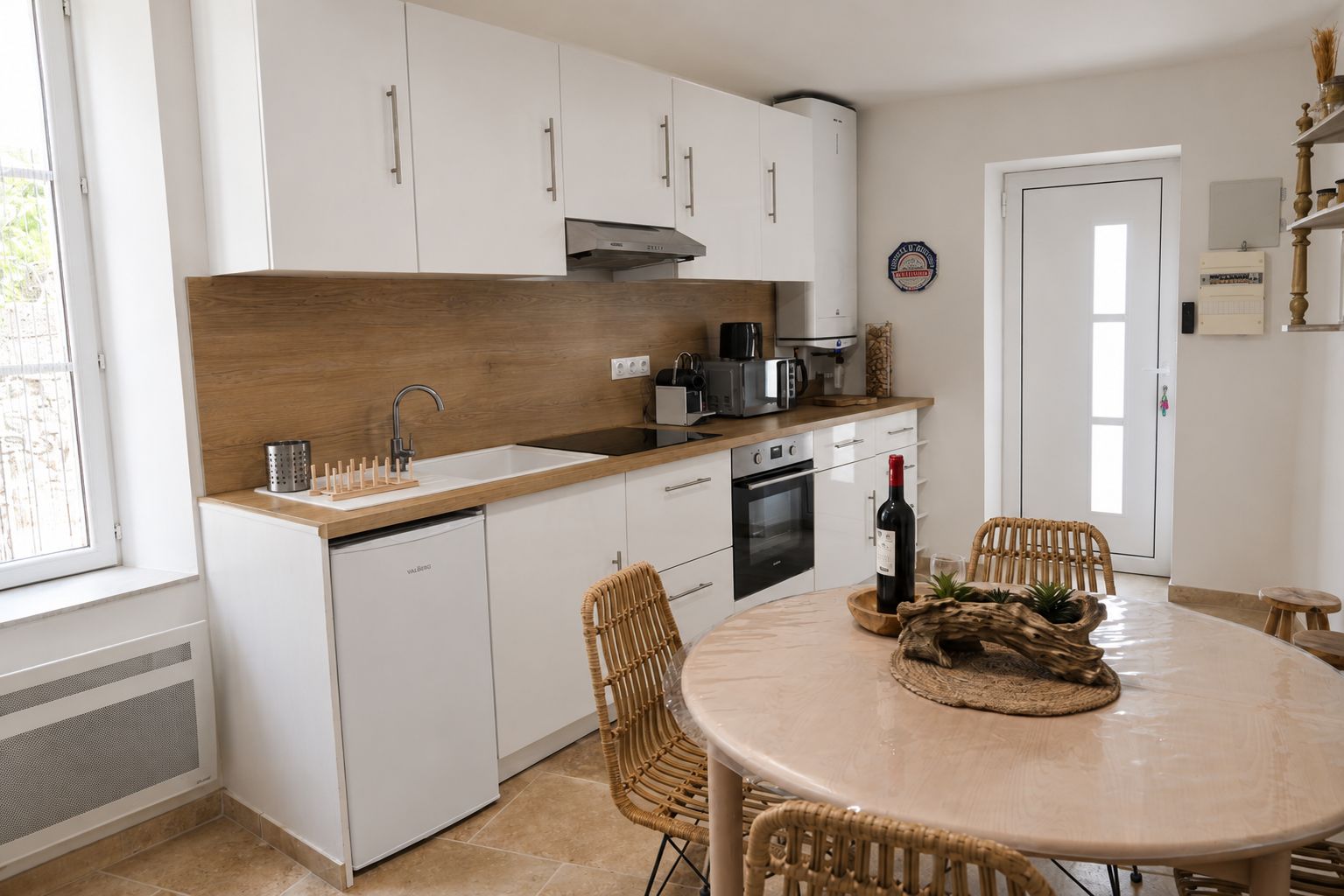 A modern kitchen with white cabinets, a built-in oven, and a dining area with wicker chairs.