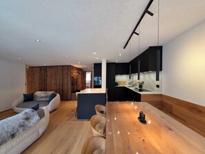 A modern living space with a wooden floor, a dining area with a wooden table, and a kitchen with black cabinets. - Du Glacier B3 Appartement/Fewo Appartement/Fewo by Interhome (Saas-Fee)