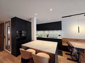 A modern kitchen with a central island, black cabinetry, and a wooden dining area. - Du Glacier B3 Appartement/Fewo Appartement/Fewo by Interhome (Saas-Fee)