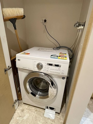 Eine kompakte Waschmaschine mit Bedienfeld, einer Steckdose und einem Schlauch an der Wand.