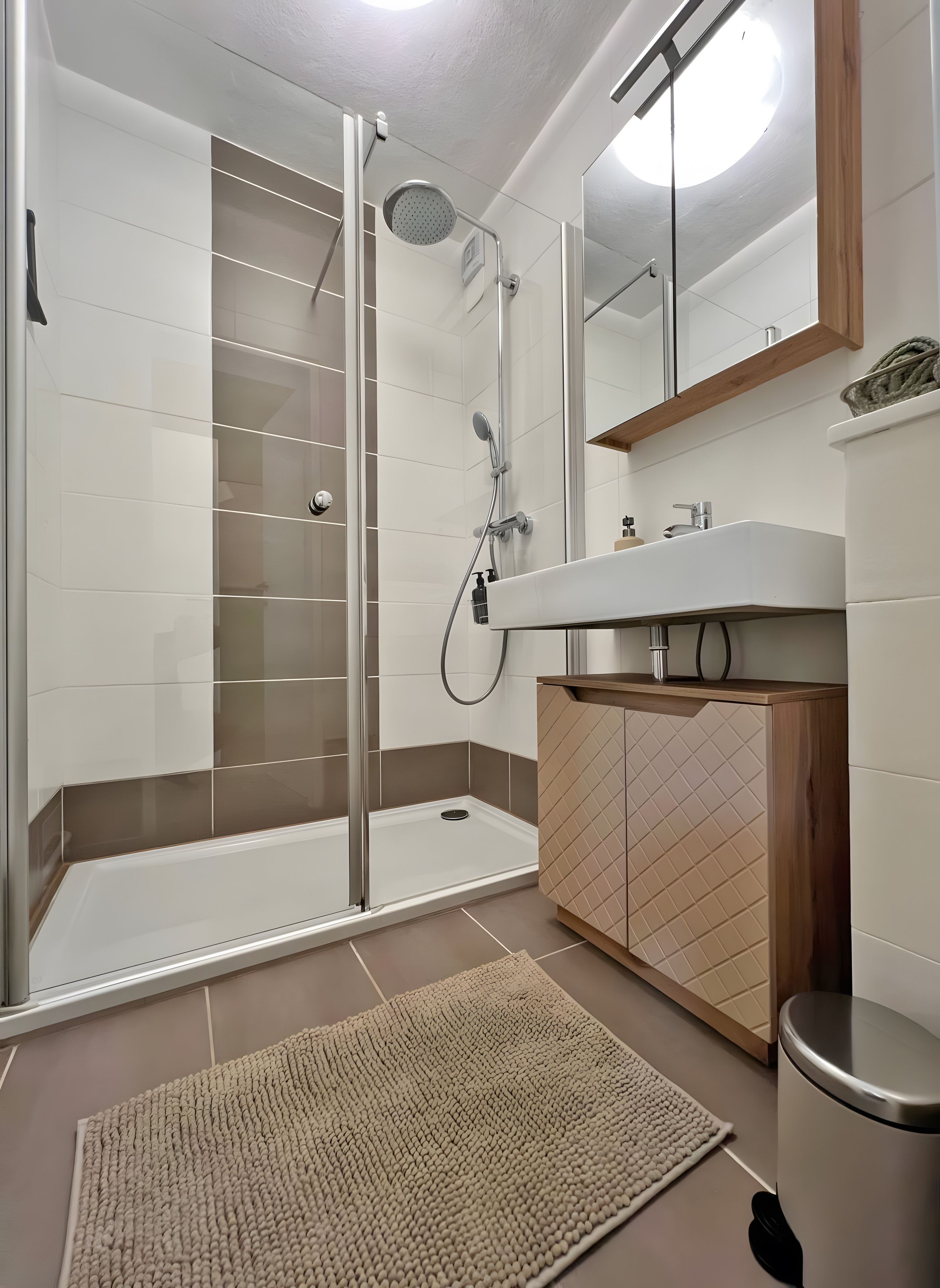 A modern bathroom with a glass shower enclosure, a wooden vanity, and a large mirror.