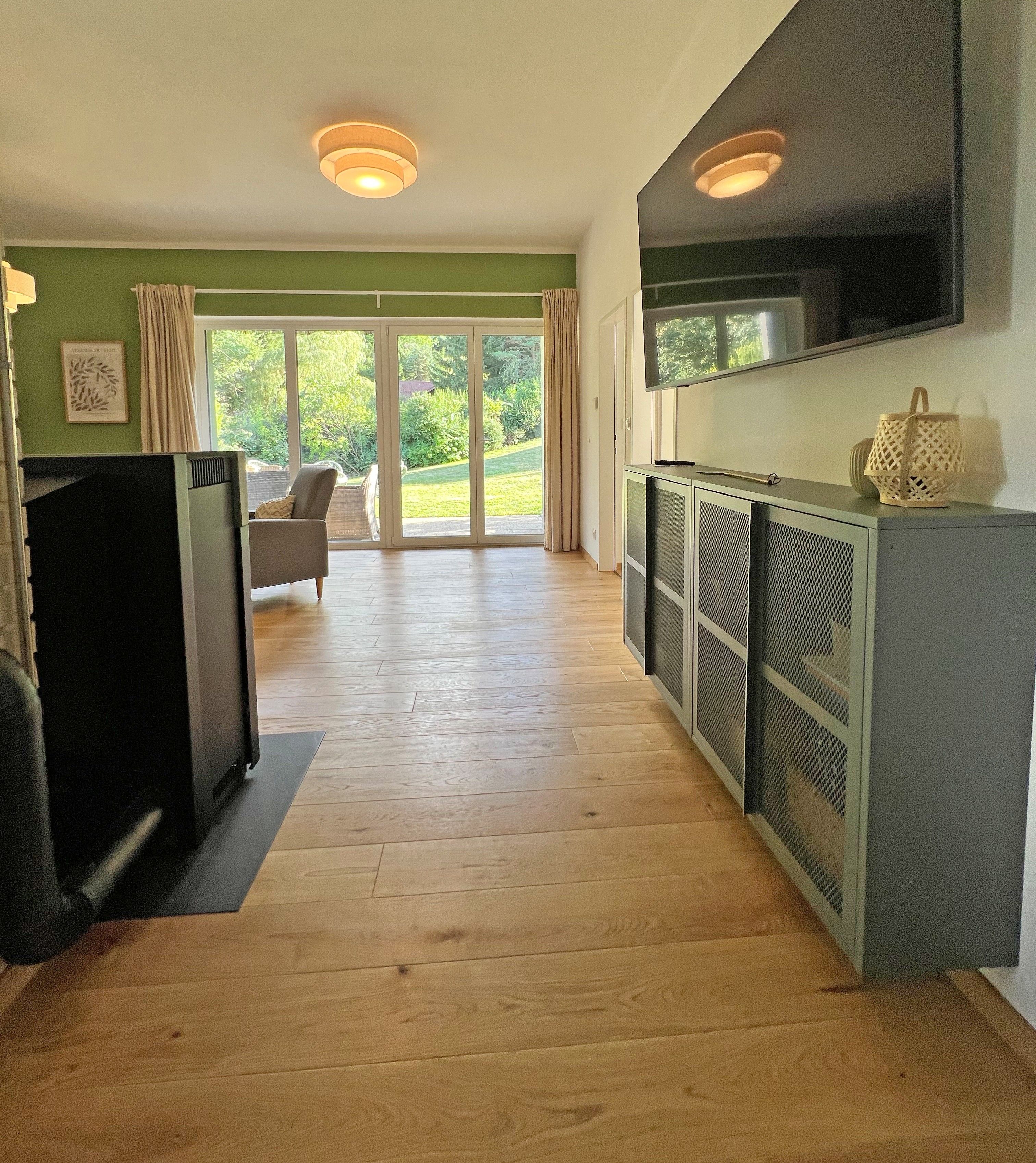 Ein Zimmer mit Holzboden, Fernseher, einer Couch und einer Schiebetür zu einem Garten.
