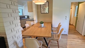 A dining area with a wooden table, chairs, a hanging light fixture, and a framed quote on the wall.