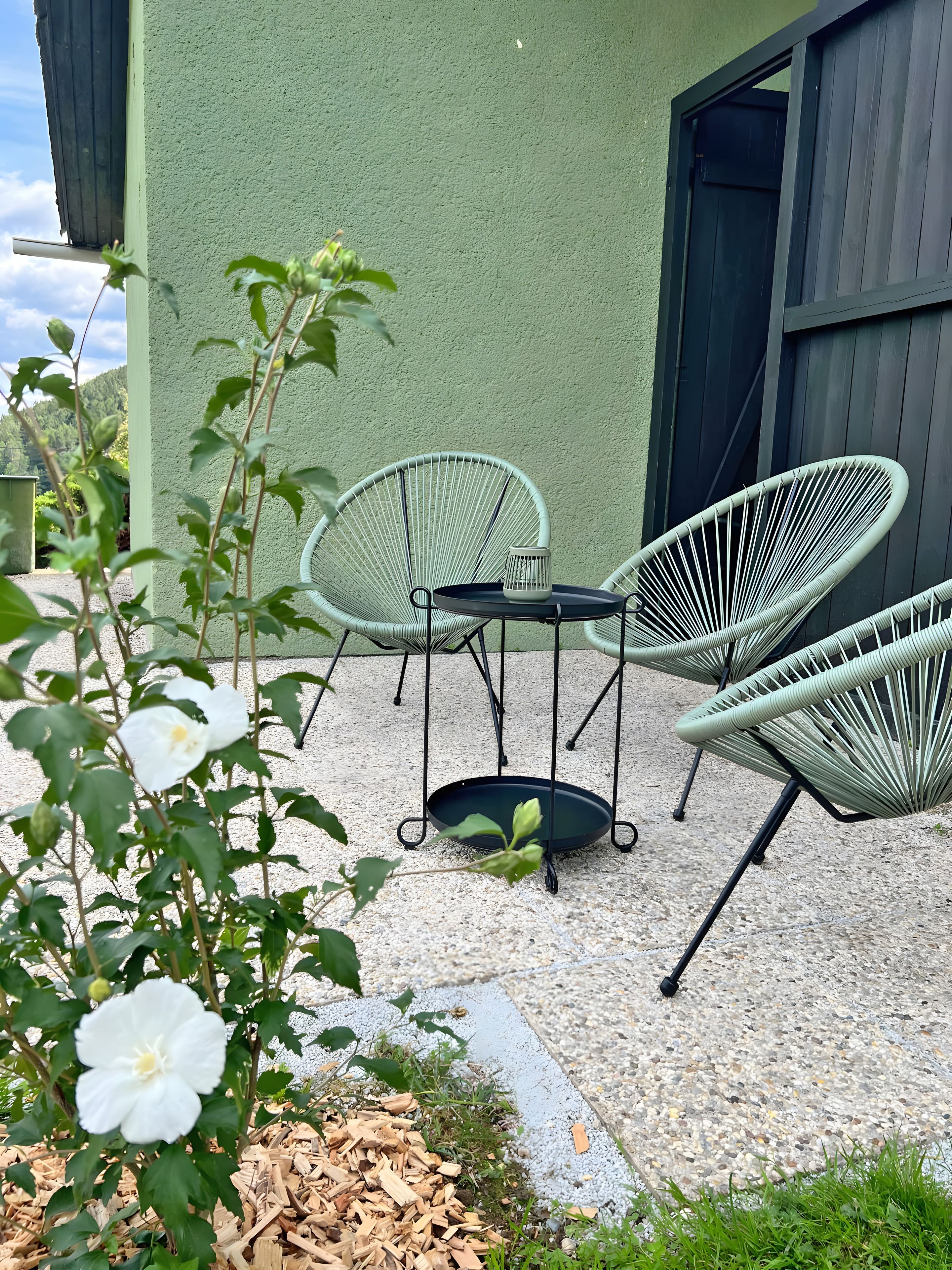 Een terras met buitenmeubilair, een kleine tafel en een hangstoel.