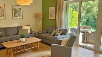 En moderne stue med sofasæt, sofabord og lænestol. Der er en gulvlampe og et billede på væggen.