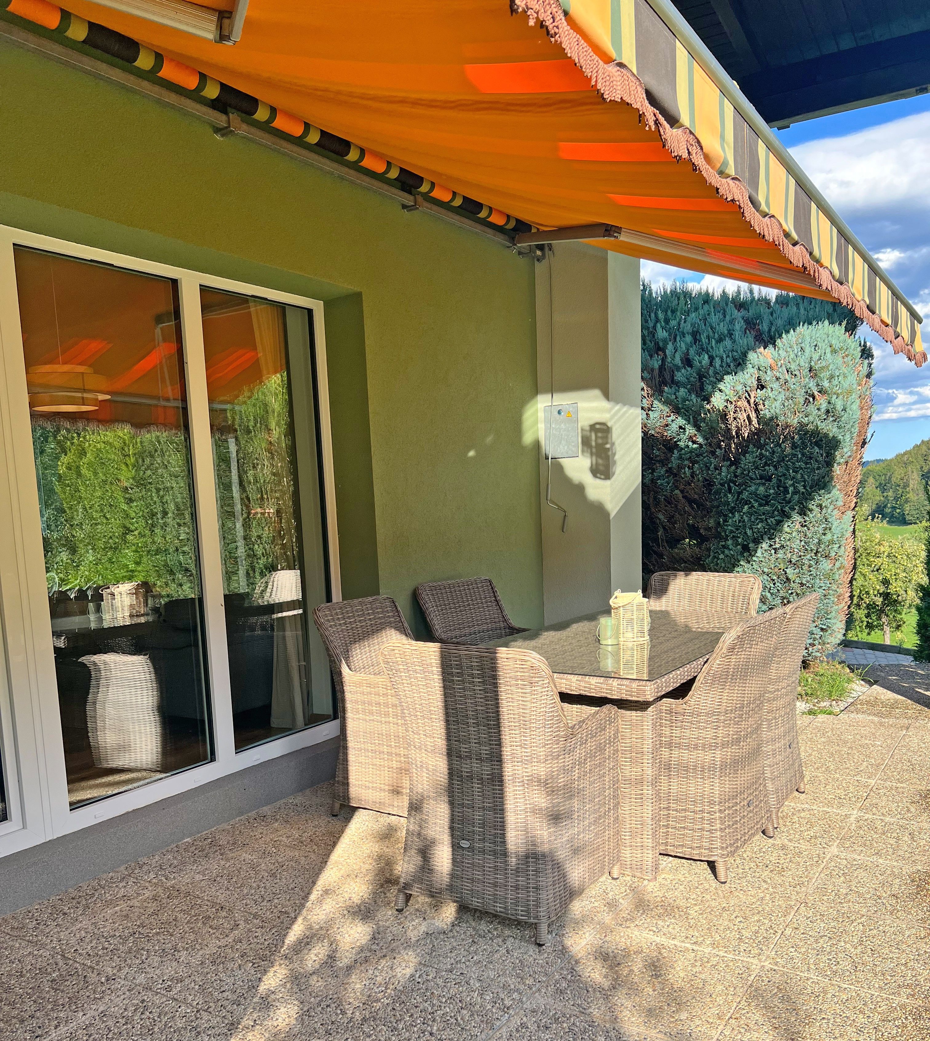 An outdoor patio with wicker furniture, a table, and a covered area with a striped awning.