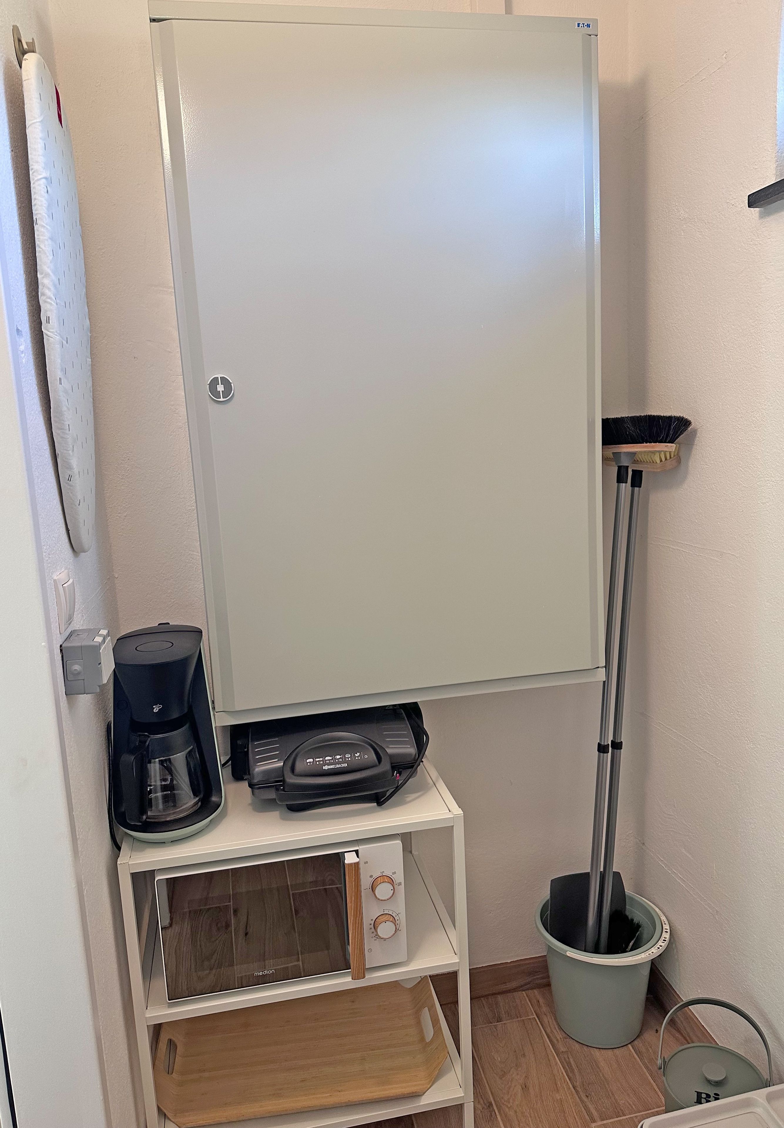Een kitchenette met een koffiezetapparaat, een magnetron en een bezem.