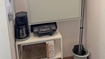 Een kitchenette met een koffiezetapparaat, een magnetron en een bezem.