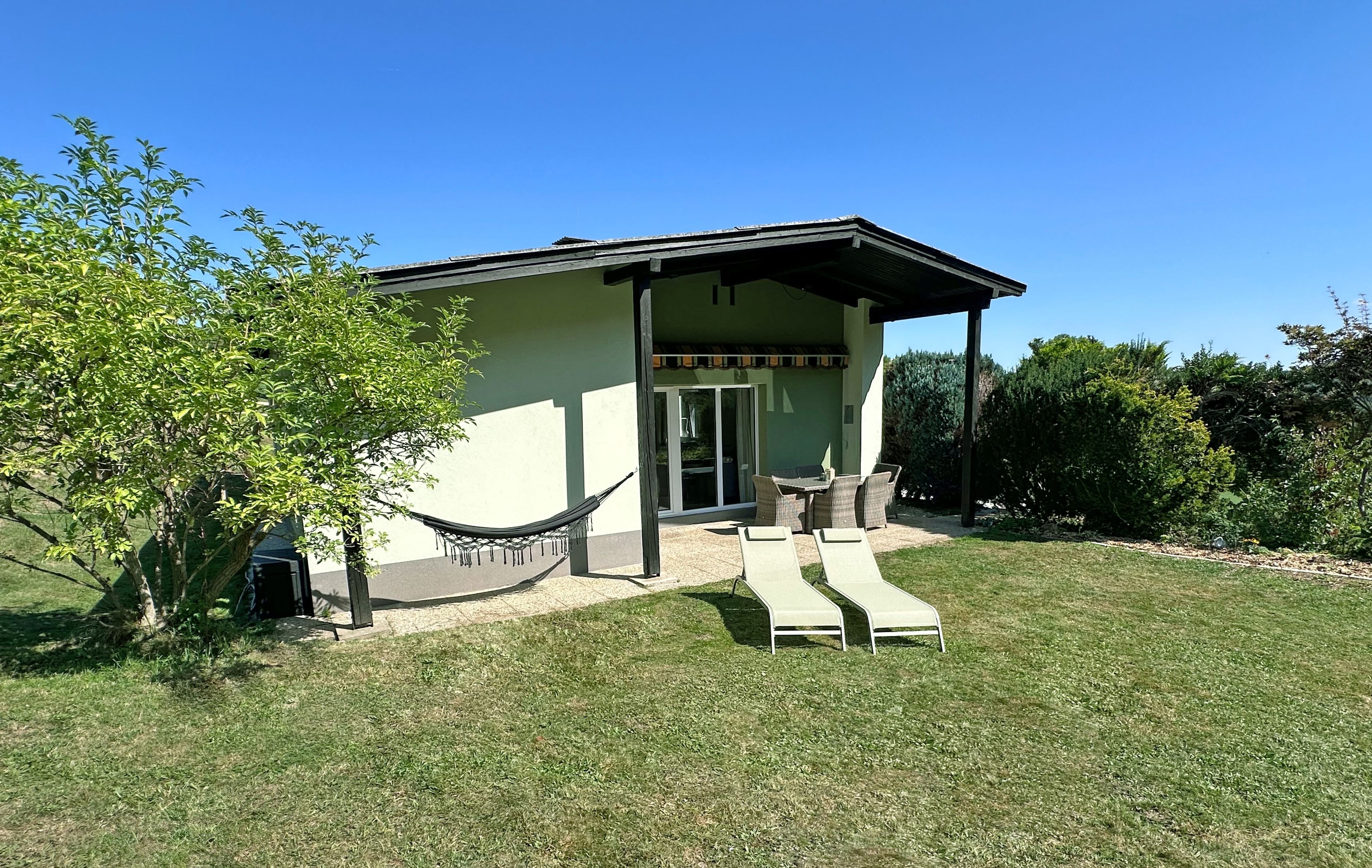 A single-story building with a covered patio area, a hammock, and two lounge chairs.