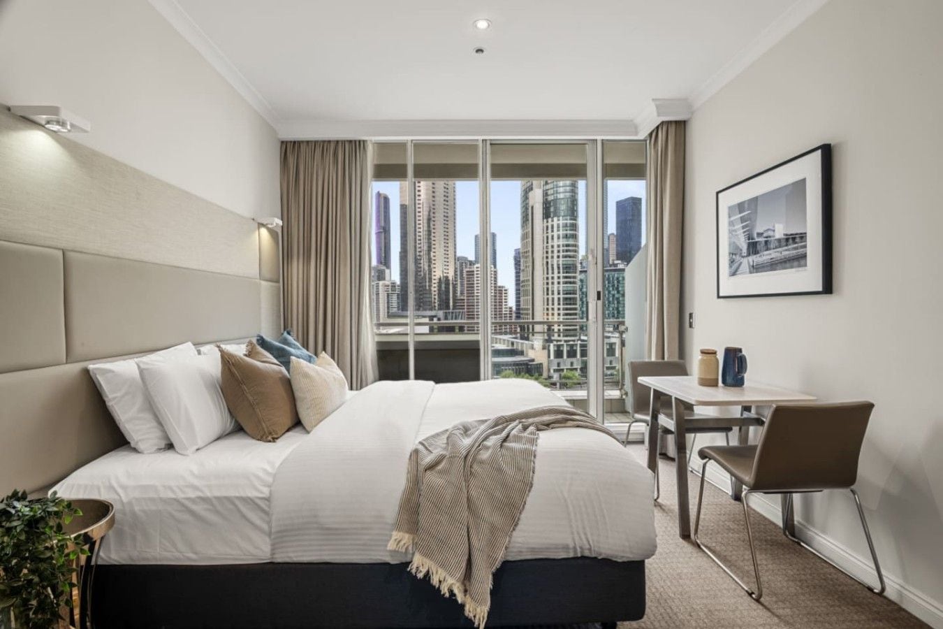 A hotel room with a large bed, a desk, and a view of a cityscape.