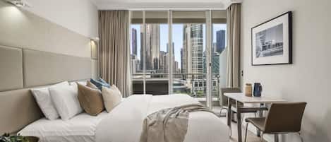 A hotel room with a large bed, a desk, and a view of a cityscape.
