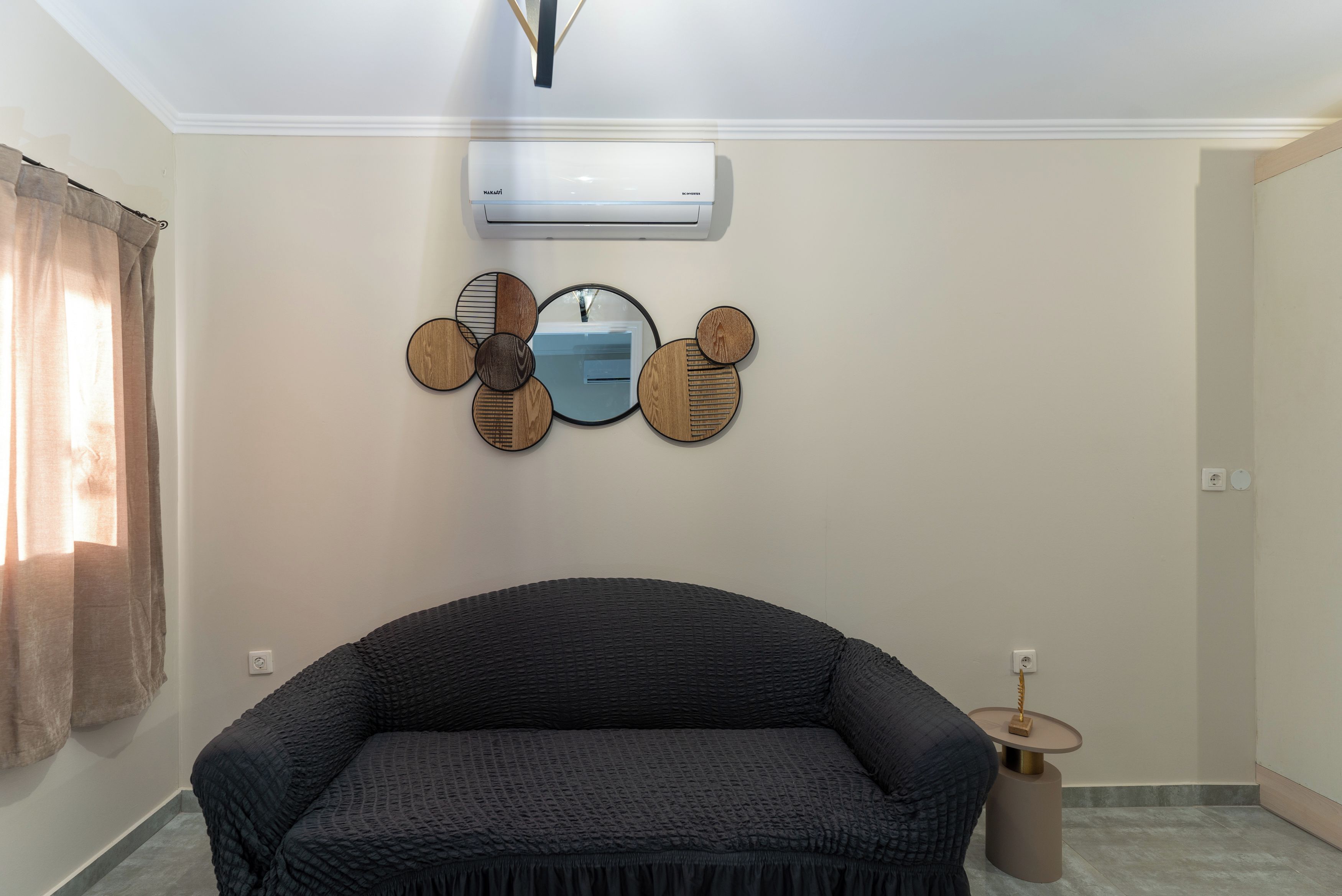 Quarto com sofá, ar-condicionado fixado na parede e um espelho decorativo.
