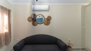 Quarto com sofá, ar-condicionado fixado na parede e um espelho decorativo.