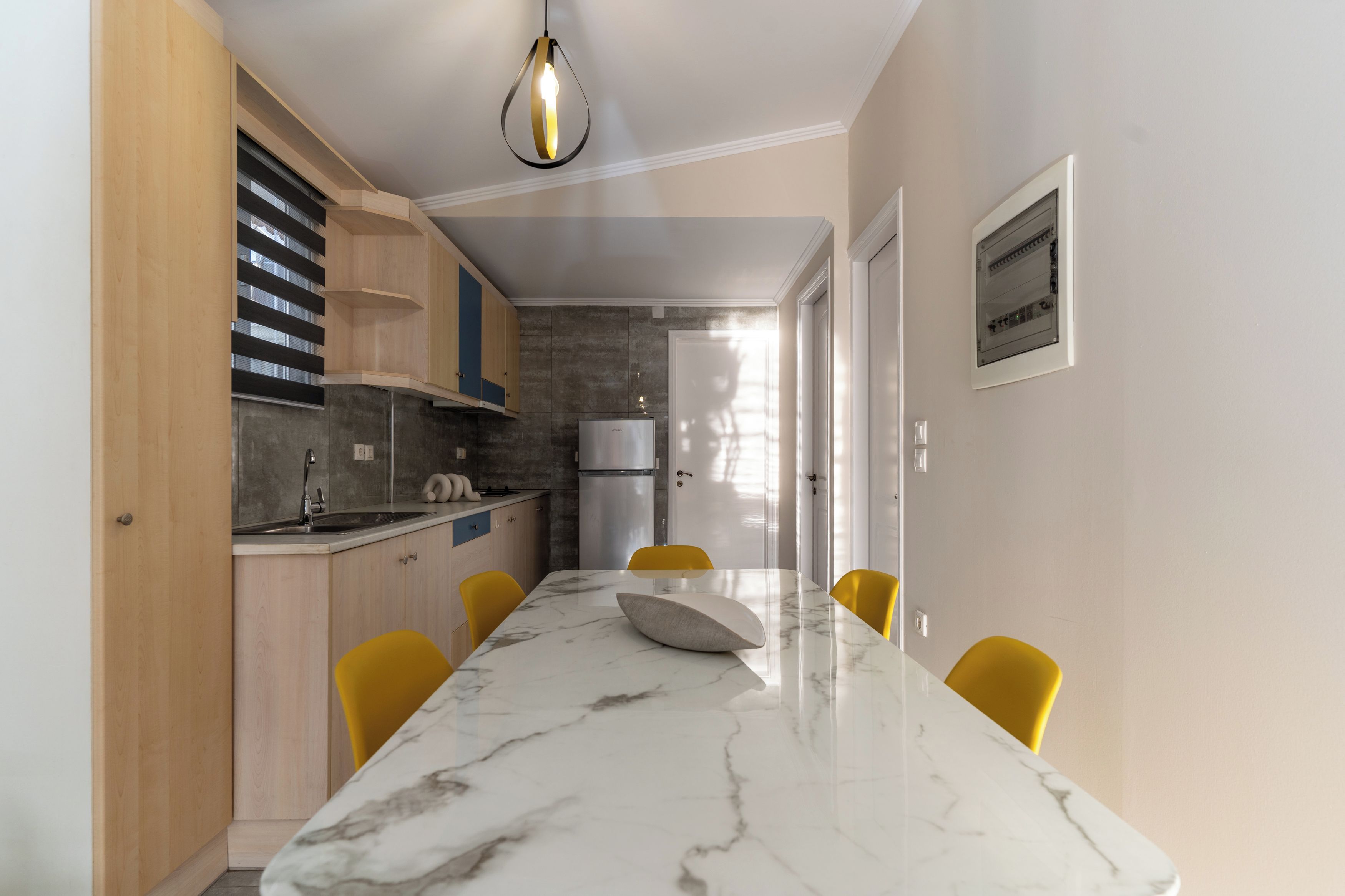A modern kitchen with a marble countertop, yellow chairs, and a pendant light.