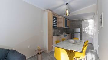 Cozinha compacta com eletrodomésticos modernos, área de jantar com cadeiras amarelas e um sofá cinza.