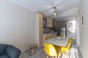 Une cuisine compacte dotée d’appareils électroménagers modernes, un coin repas avec des chaises jaunes et un canapé gris.