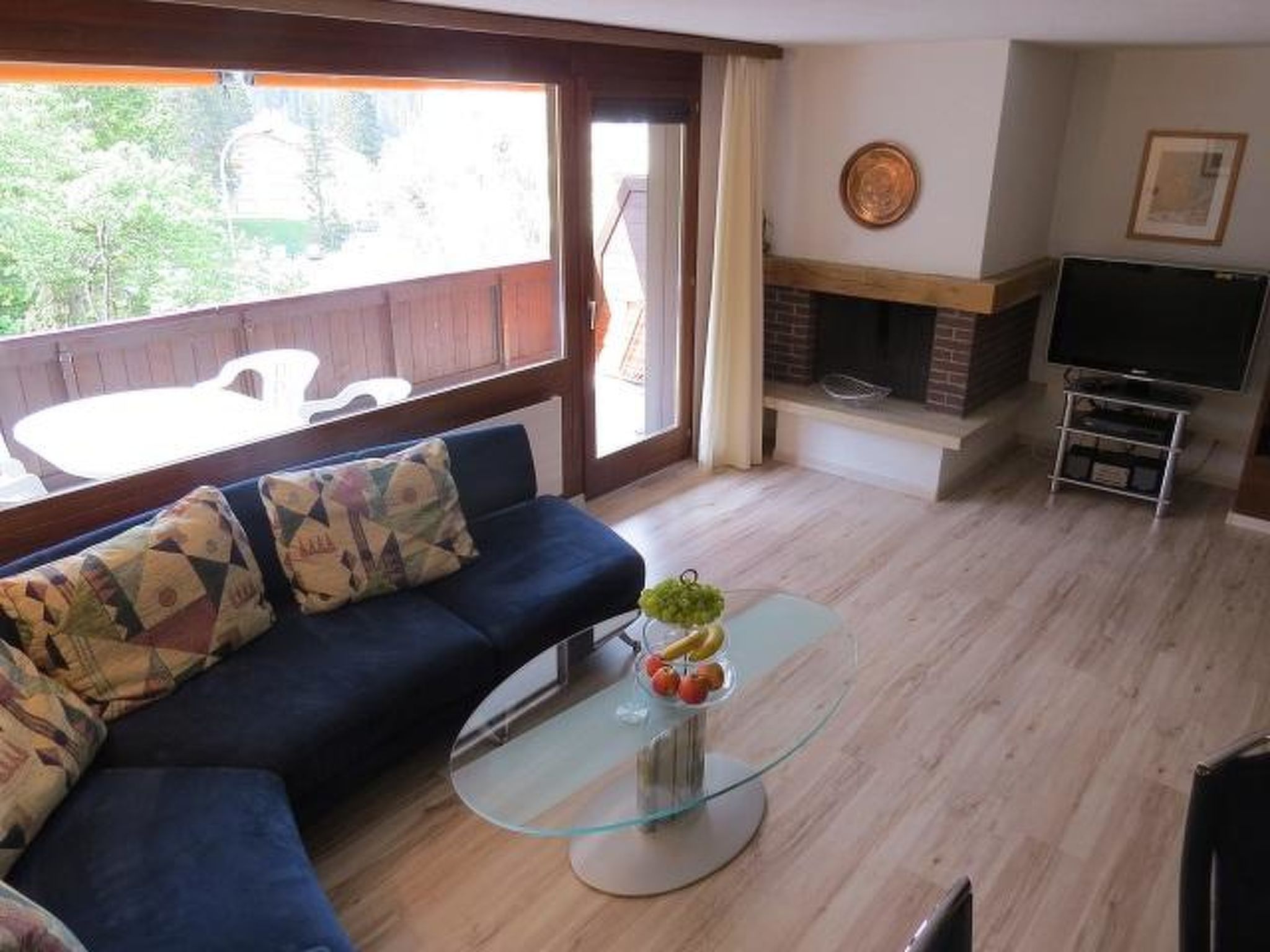 Ein Wohnzimmer mit einer Couch, einem Glastisch, einem Kamin und einem Fernseher.