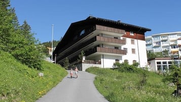 Ein Weg führt zu einem mehrstöckigen Gebäude mit Balkonen, umgeben von Grünpflanzen.