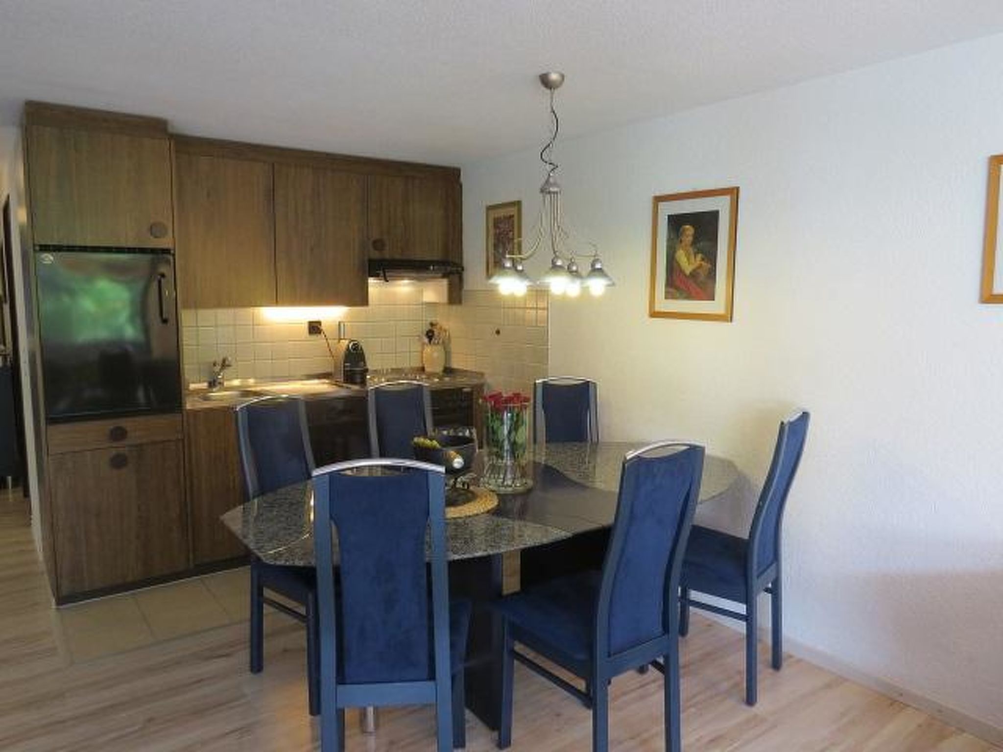A modern kitchen with wooden cabinets, a built-in refrigerator, and a dining area with a round table and chairs.