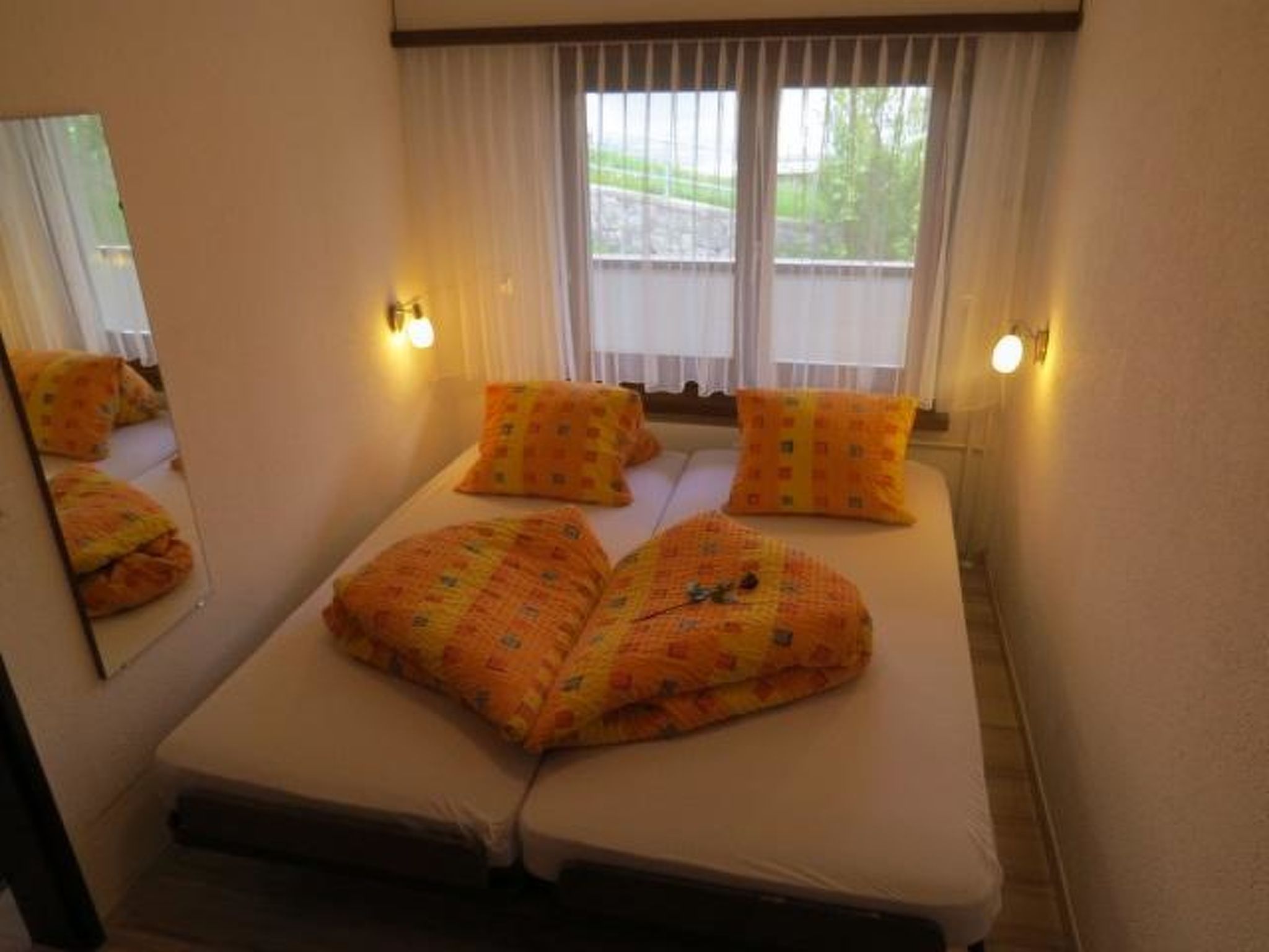 A double bed with patterned pillows, a bedside lamp, and a window with curtains.