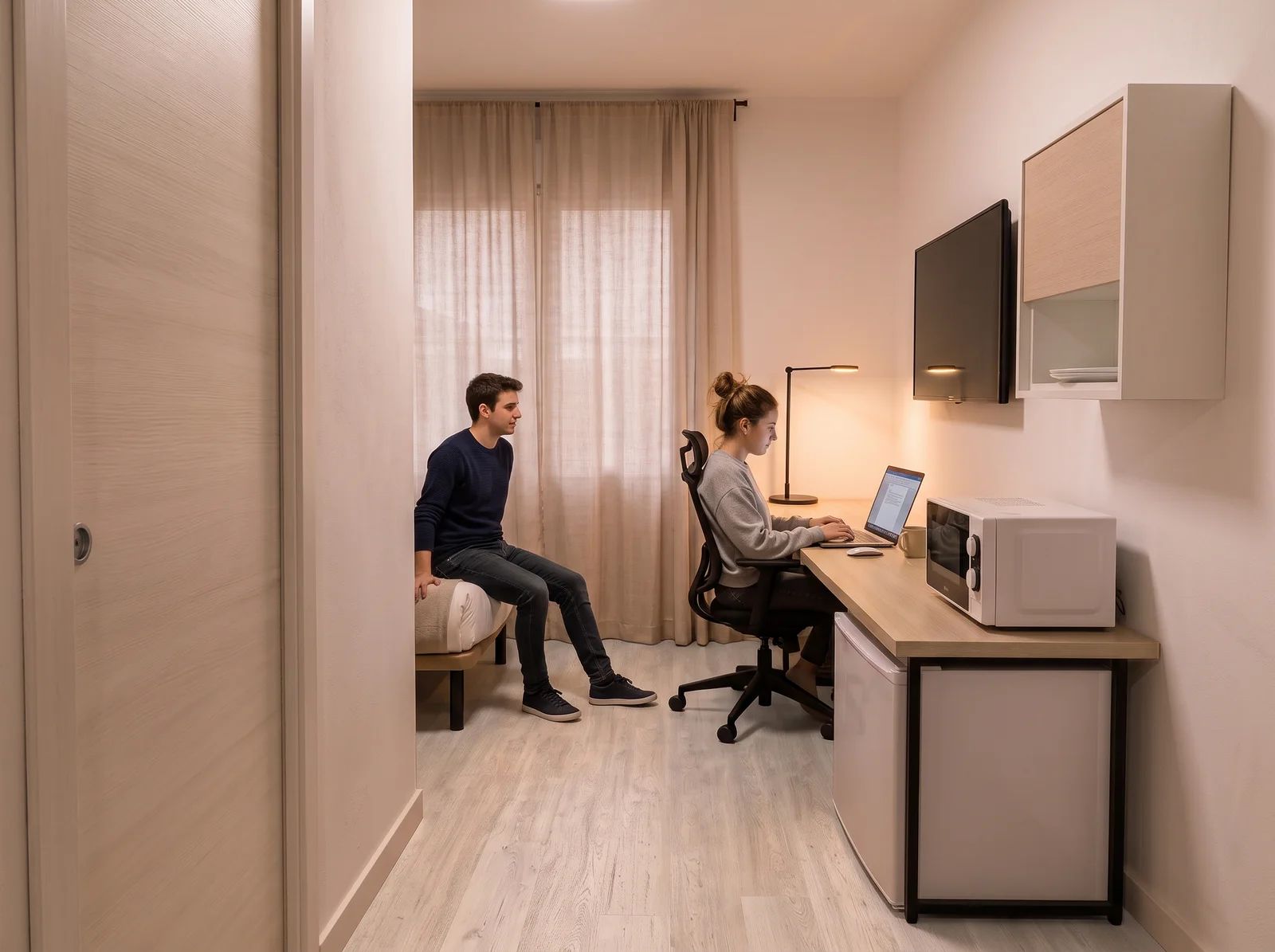Habitación compacta con cama, escritorio, silla, televisor y microondas.