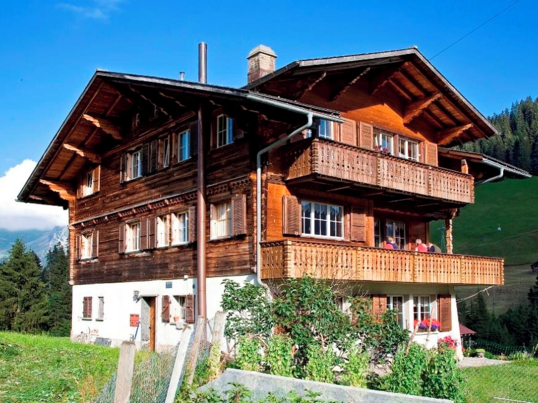 A two-story wooden chalet with a balcony, set in a mountainous area.