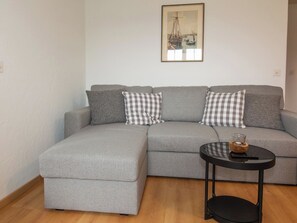 A grey sectional sofa with checkered pillows, a round black side table with a glass and candle, and a framed picture on the wall. - Chalet Gsür Appartement/Fewo, Bad, WC, 2 Schlafräume by Interhome (Adelboden)