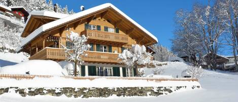 Un chalet in legno con un balcone, circondato da alberi innevati e un cielo azzurro limpido.