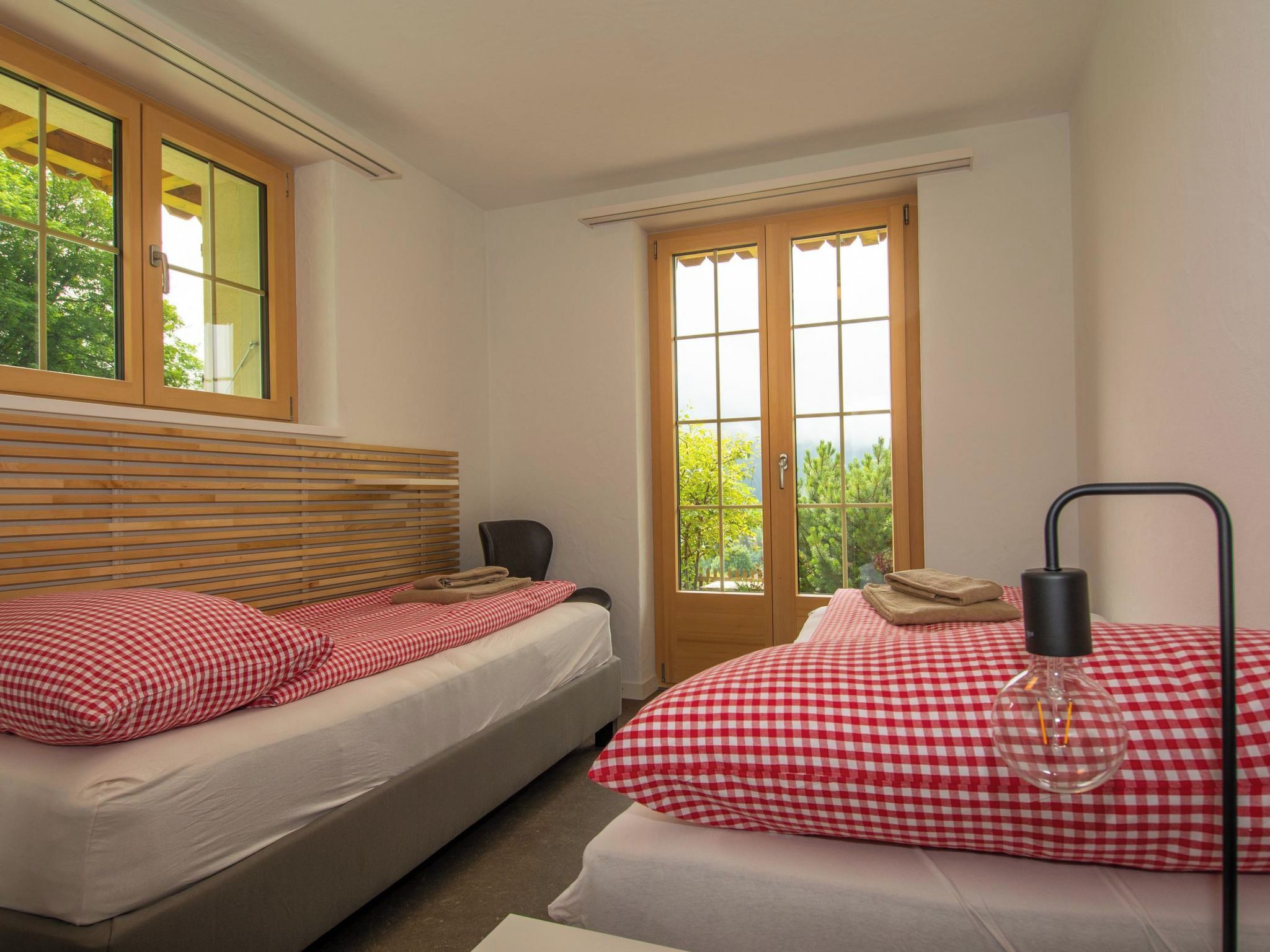 Une chambre avec deux lits, une tête de lit en bois, une fenêtre donnant sur les arbres et une lampe de chevet.