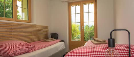 Un dormitorio con dos camas, un cabecero de madera, una ventana con vistas a árboles y una lámpara de noche.