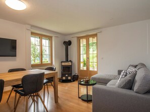 A modern living room with a wooden dining table, grey sofa, and a black wood-burning stove. - Chalet Gsür Appartement/Fewo, Bad, WC, 2 Schlafräume by Interhome (Adelboden)