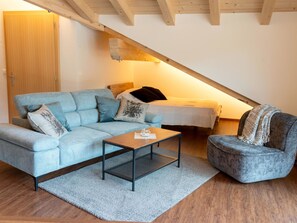 Ein gemütliches Schlafzimmer im Loft-Stil mit schrägverdeckter Decke, einem Bett, einer Couch und einem Sessel.