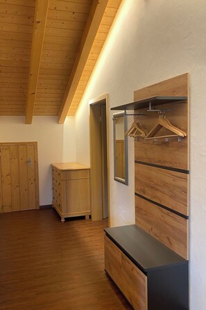 Ein Zimmer mit Holzboden, einem Holzschrank, einem schwarzen Konsolentisch und einer an der Wand befestigten Holzvertäfelung mit Spiegel und Kleiderstange.